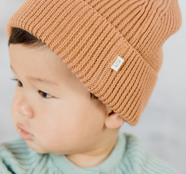 Picture shows baby boy wearing organic cotton rib knit beanie in Acorn color. 