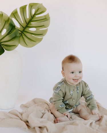 Baby boy wearing organic cotton knit cardigan in sage green with jacquard zebra pattern and magnetic button closures.