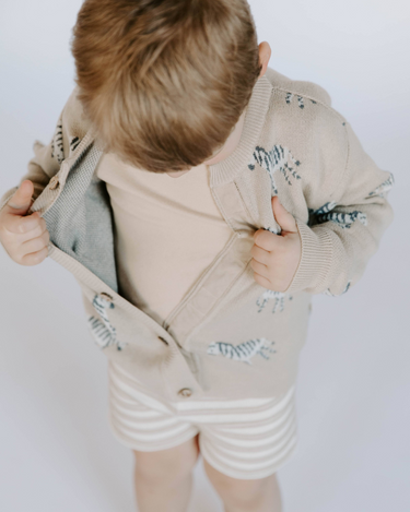 Little boy wearing organic cotton knit cardigan in mushroom beige with jacquard zebra pattern and magnetic button closures.