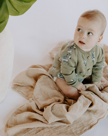 Baby boy wearing organic cotton knit cardigan in sage green with jacquard zebra pattern and magnetic button closures.