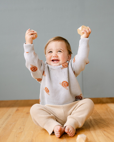 Image shows baby boy wearing organic cotton knit sweater with jacquard snail pattern in pearl blue. 