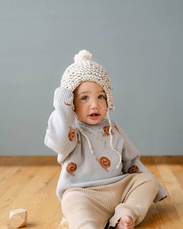 Image shows baby boy wearing organic cotton knit sweater with jacquard snail pattern in pearl blue. 