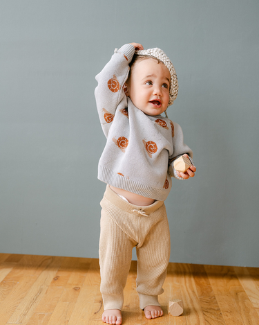 Image shows baby boy wearing organic cotton knit sweater with jacquard snail pattern in pearl blue. 