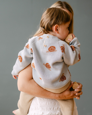 Image shows baby boy wearing organic cotton knit sweater with jacquard snail pattern in pearl blue. 