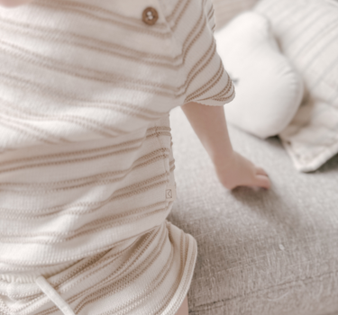 Image shows close up shot of toddler girl wearing organic cotton stripe knit set in mushroom.