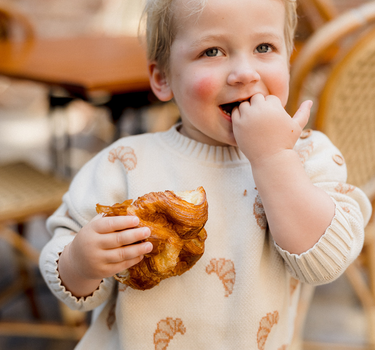 Picture shows little boy wearing organic cotton knit sweater with croissant pattern and magnetic buttons at neck.