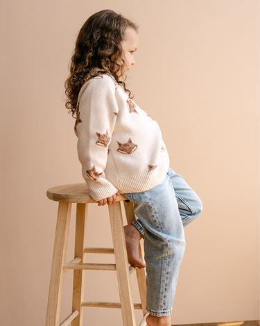 Image shows little girl wearing organic cotton knit sweater with jacquard fox pattern in pale pink. 