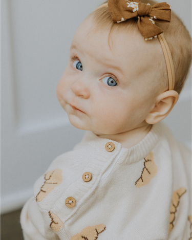 Baby girl wearing organic cotton knit croissant patterned sweater with Magnetic Button closures at the neck. 
