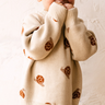 Image shows toddler boy wearing organic cotton knit sweater with snail jacquard pattern in oatmeal. 